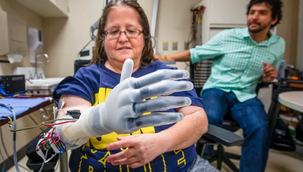 Karen Sussex, an upper-limb amputee from Jackson, Mich., operates a Touch Bionics I-LIMB prosthetic hand as Alex Vaskov, robotics Ph.D. candidate, looks on during a testing session at a lab in the University of Michigan Hospital in Ann Arbor, MI on June 13, 2019, for an advanced prosthetics study at U-M.