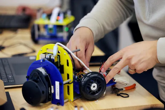 Two hands work on small robot on a bench top.