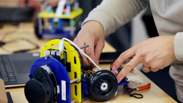 Two hands work on small robot on a bench top.