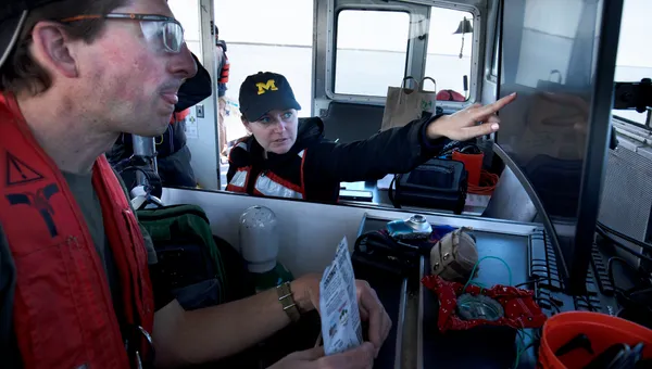 Two researchers on a boat, as one of them points to the sonar data they are collecting on a screen.