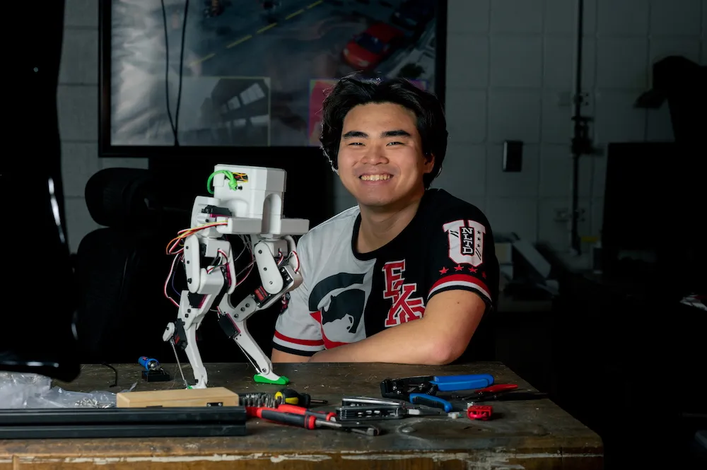 David Ho sits at a workbench with the Legolas bipedal robot