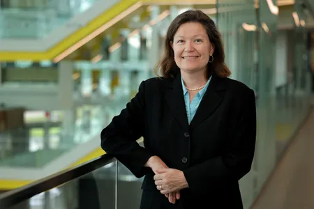 Dawn Tilbury smiles while leaning on a glass railing in the atrium of the Ford Robotics Building.