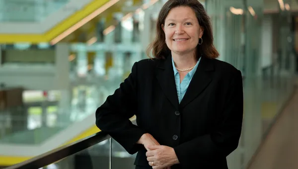 Dawn Tilbury smiles while leaning on a glass railing in the atrium of the Ford Robotics Building.