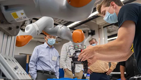 A robot arm grasps a rope as a researcher assists.