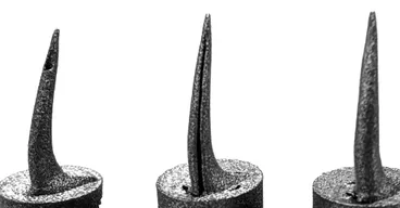 Three 3D-printed titanium snake fangs side by side, each with a different venom channel structure, mounted on cylindrical bases.