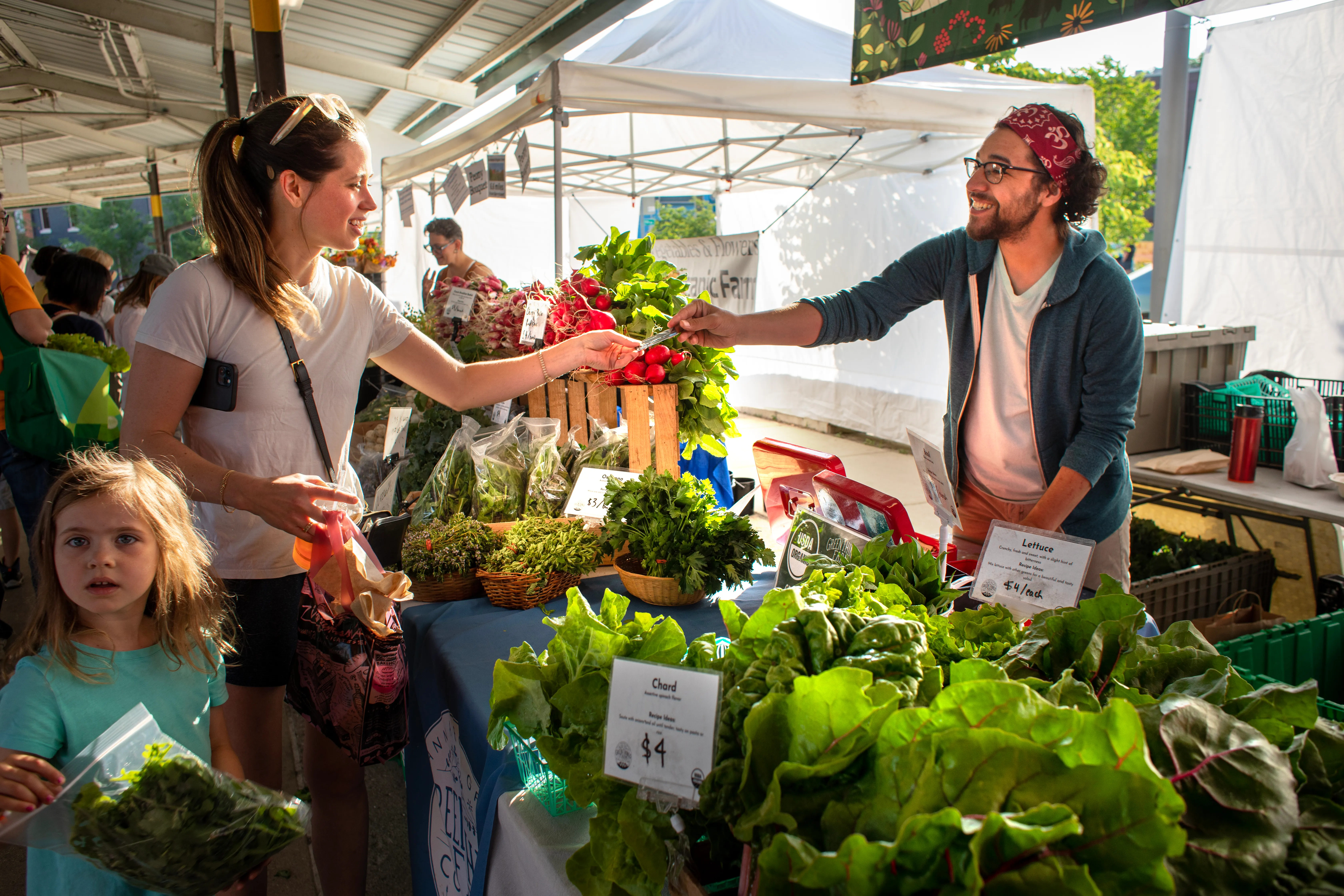 People browsing tables of fresh produce at an outdoor market.