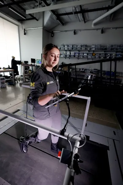 A researcher walks on a treadmill while wearing a pair of ankle exoskeletons.