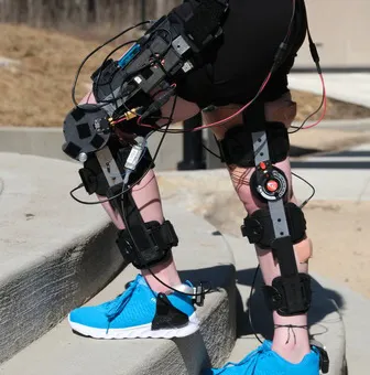 A person wearing a knee exo standing across stairs outside.