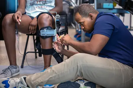 A researcher adjusts a robotic knee joint brace on a test subject