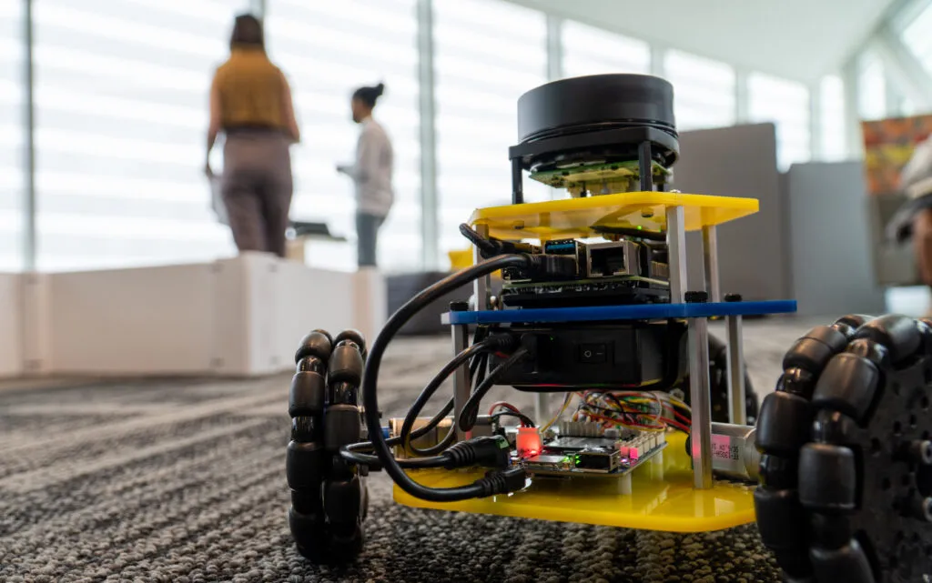 A small classroom robot with three wheels is has its LEDs lit up as it waits for a command.