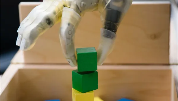 Close up of advanced prosthetic hand with a green block grasped between the thumb and index finger, positioning the block at the top of a stack.