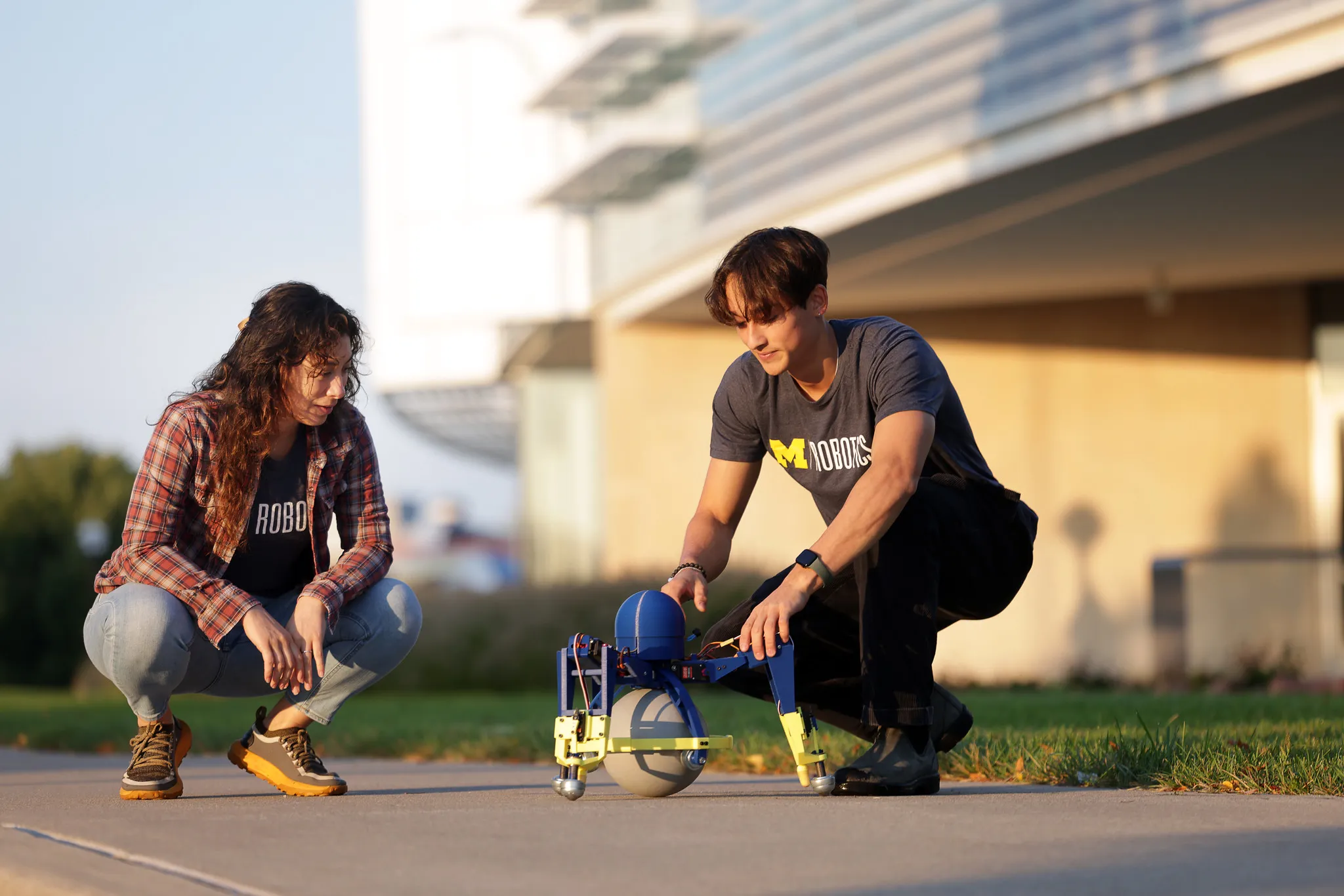 A professor and undergraduate student work on a bio-inspired robot resembling an octopus sitting on a ball outside of the Robotics Building