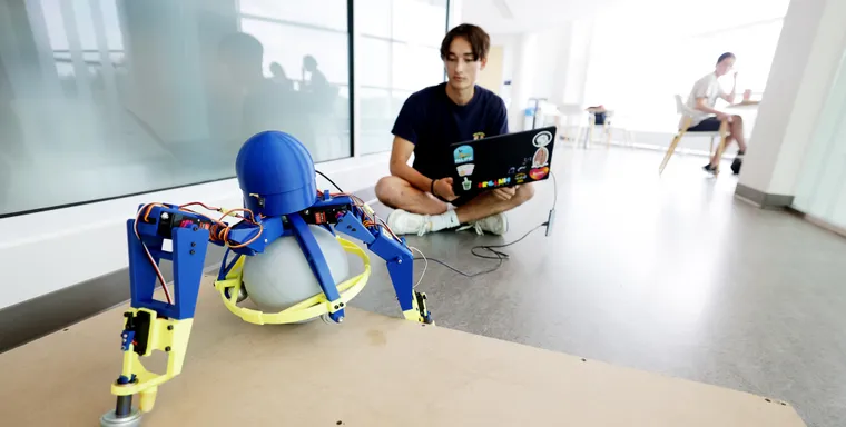 Adam Hung, Robotics undergraduate, with a tripedal robot he developed at the Ford Robotics Building.