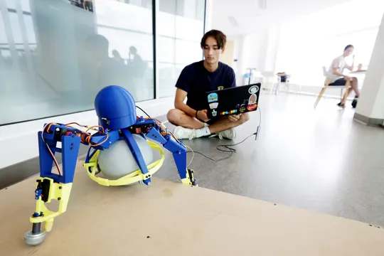 Adam Hung, Robotics undergraduate, with a tripedal robot he developed at the Ford Robotics Building.