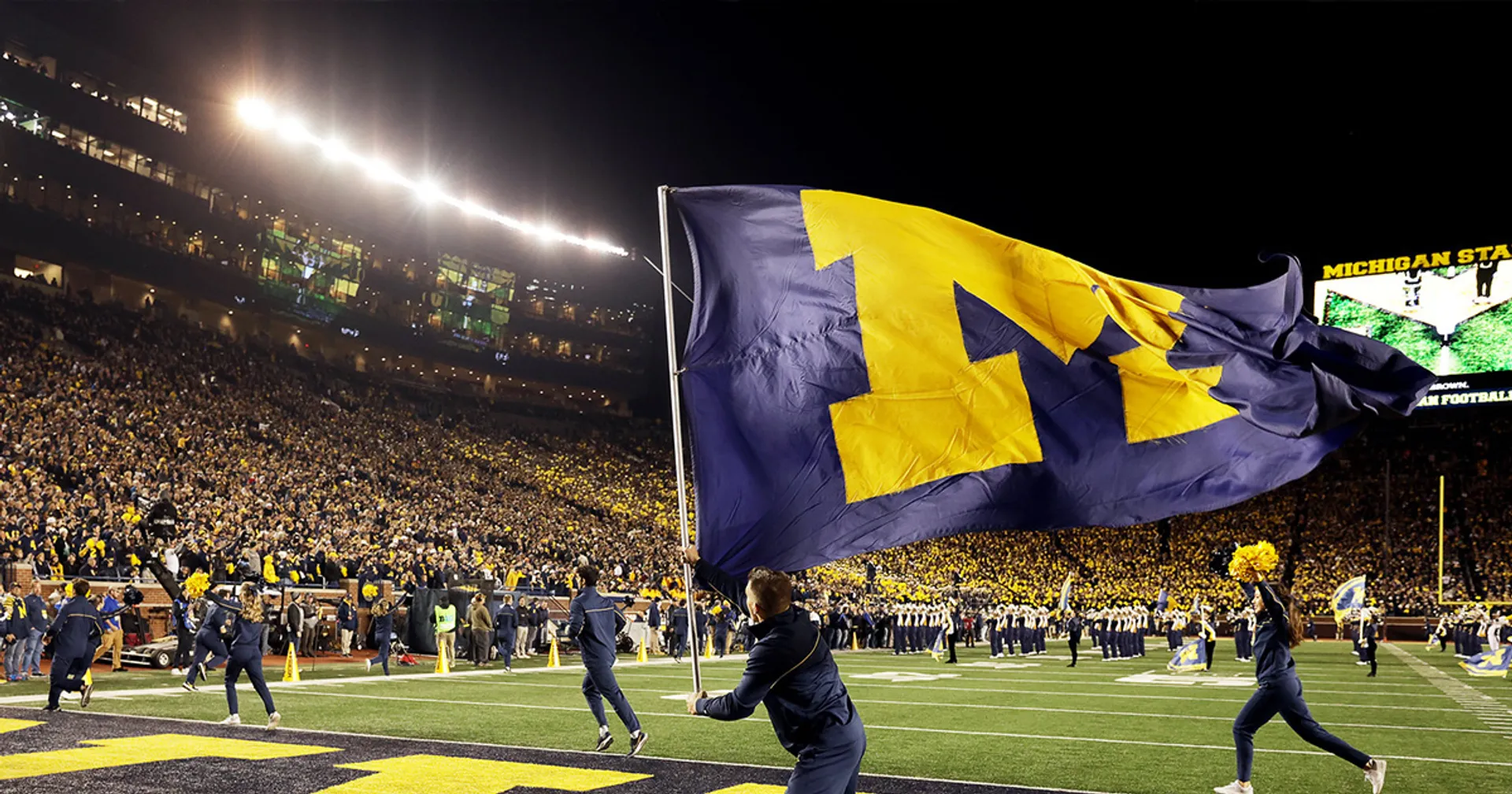 A gigantic U-M flag is waved in the Big House football stadium