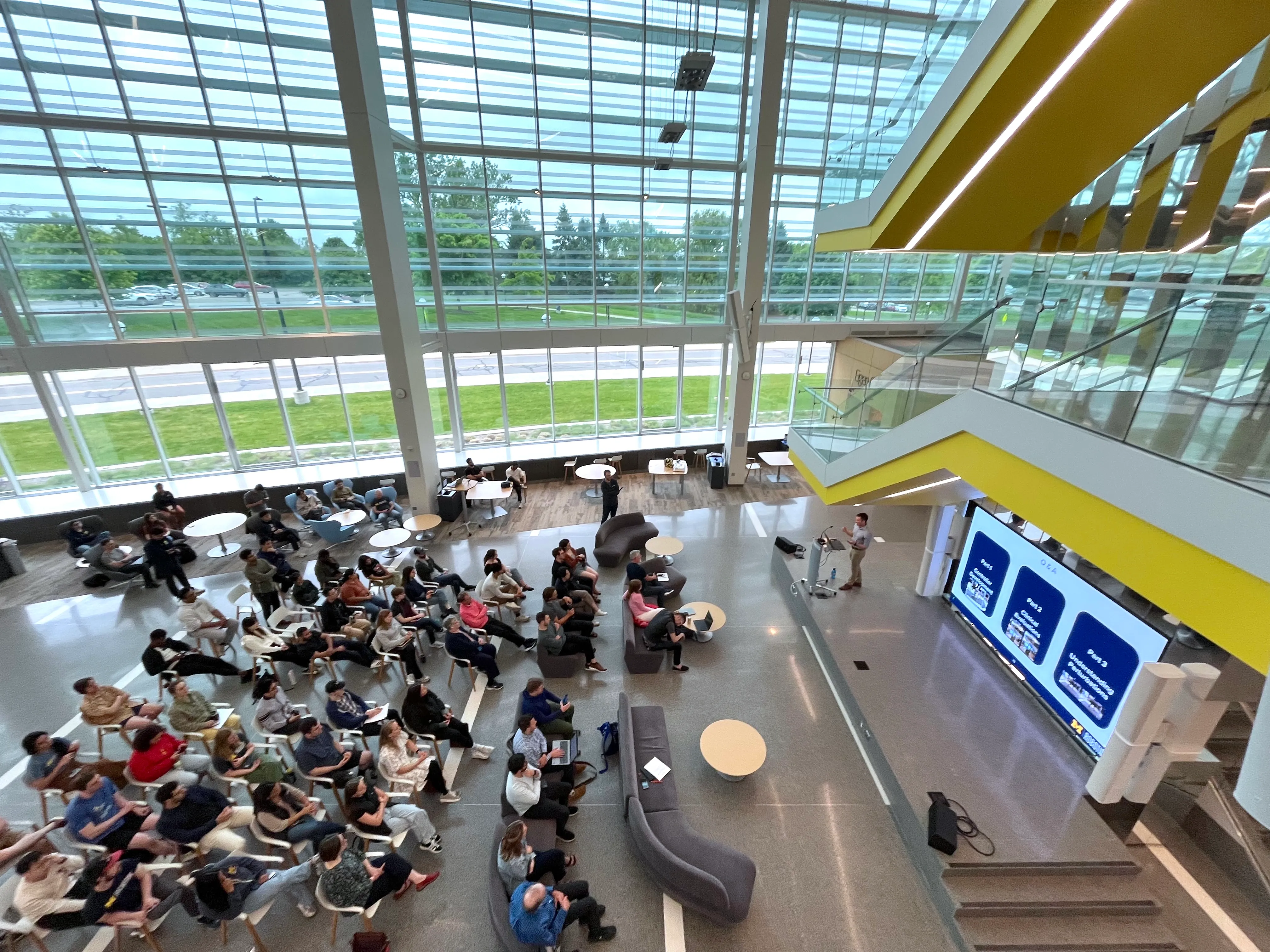 A PhD candidate defends their dissertation in the atrium of the Ford Robotics Building